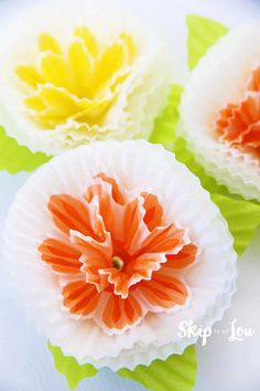 three paper flowers sitting on top of a white plate with green and yellow leaves around them