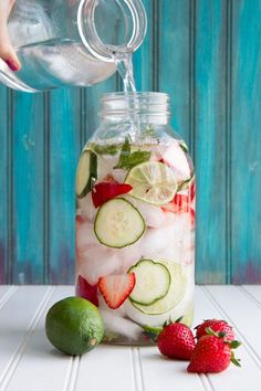 a person pouring water into a jar filled with cucumbers and strawberries