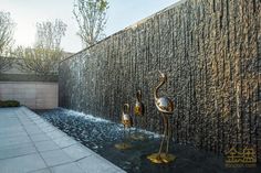 two flamingos are standing in front of a wall that has water running from it