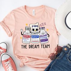 a pink shirt that says the dream team with two cats on it next to sunglasses and hat