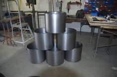 several metal pots are stacked on top of each other in a workshop area with workbench and tools behind them