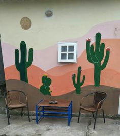 two chairs and a table in front of a painted wall with cacti on it