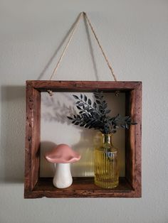 a wooden frame hanging on the wall with two vases and a plant in it