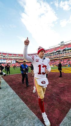 a football player is running on the field with his arm in the air and one hand up