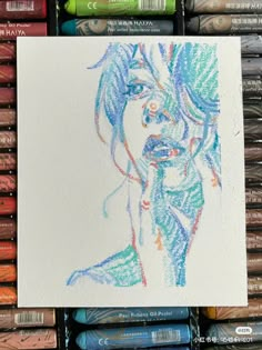 some crayons are next to a drawing of a woman's face with blue hair