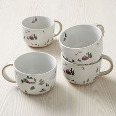 three white cups sitting on top of a table next to each other with trees and mountains painted on them