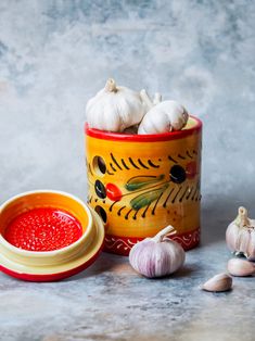 garlic and red sauce in a yellow bowl next to garlic cloves on a table