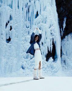 a woman standing in front of an ice covered waterfall with her arms up and legs crossed