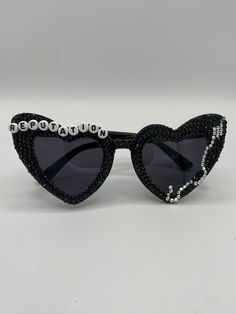 a pair of heart shaped sunglasses with black and white crystals on the lens, both decorated with beads