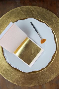 a white plate topped with a piece of paper next to a paintbrush and card