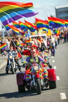 a group of people riding motorcycles down a street with rainbow flags in the back ground