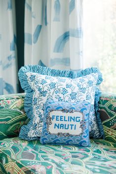 a blue and green couch with pillows on it in front of a curtained window