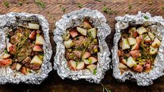 three tin foil trays filled with food on top of a wooden table next to each other