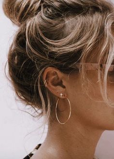 a woman with blonde hair wearing gold hoop earrings and a black top knoted into her bun