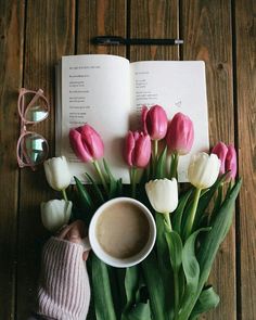 there is a cup of coffee next to some flowers and a book on the table