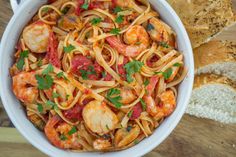 a bowl of pasta with shrimp, tomatoes and parmesan bread on the side