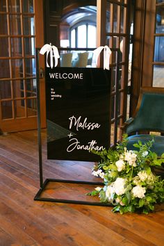 a welcome sign with flowers in front of it on the floor next to a chair