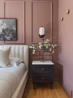 a white bed sitting next to a nightstand with flowers on it in front of a pink wall