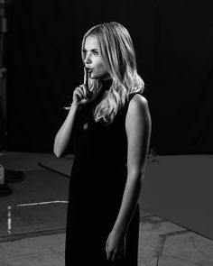 a woman standing in front of a black backdrop talking on a cell phone with her hand to her mouth