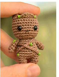 a tiny crocheted creature is being held in someone's hand with green eyes