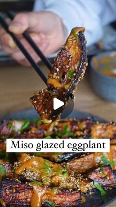 someone is eating food with chopsticks on a plate that says miso glazed eggplant