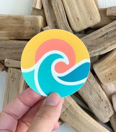 a hand holding up a sticker with an ocean wave on it