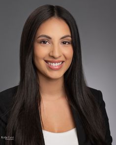 a woman with long black hair smiling at the camera and wearing a blazer jacket