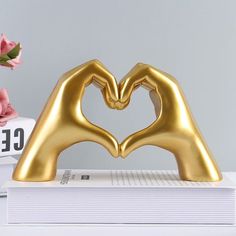 two gold hands making a heart shape on top of a stack of books