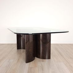 a glass and metal table with two circular bases on wooden floors in front of a white wall