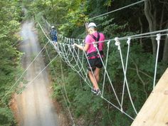 a woman walking across a suspension bridge in the woods