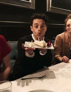 three people sitting at a table with cake in front of them and one person holding a piece of cake