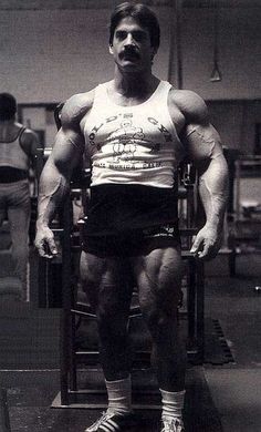 a man standing on top of a bench with his hands in his pockets and muscles