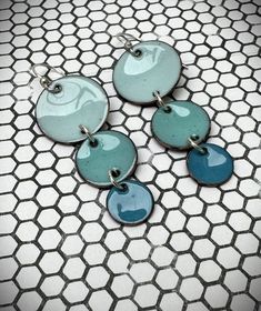 three blue and green earrings sitting on top of a tiled floor