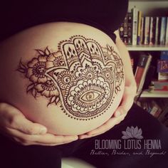 a pregnant woman's belly with henna tattoo on her stomach in front of a bookshelf