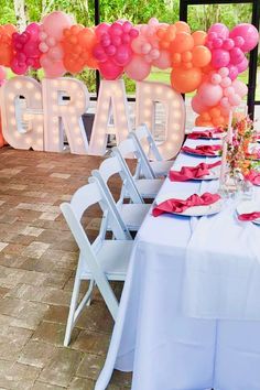 a table set up for a graduation party with pink, orange and white balloons on it