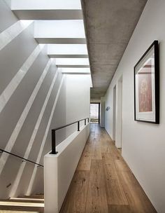 a long hallway with white walls and wooden flooring next to a stair case in an apartment