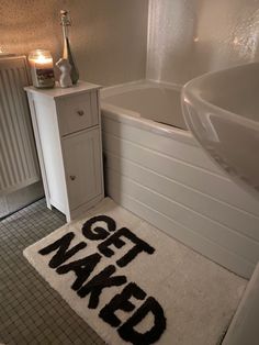 a bathroom with a rug that says get naked next to a bathtub and sink