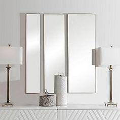 a white dresser topped with two lamps and mirrors