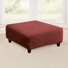 a red ottoman sitting on top of a carpeted floor next to two large windows