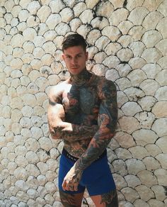 a man with tattoos standing in front of a stone wall