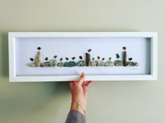 a person is holding up a shadow box with rocks and plants in it that spell out the word love