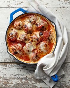 a casserole dish with meatballs and sauce in it on a white wooden table