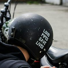 a person wearing a black helmet sitting on a motorbike with the words loud pipes save lives written on it