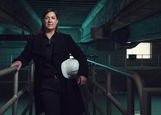 a woman in black coat and white helmet standing on metal handrails near railing