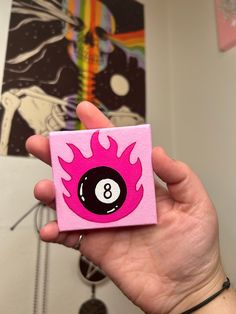 a person holding up a pink and black eight ball pin with flames on the front