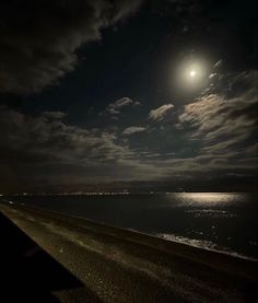 the full moon shines brightly over the ocean and beach at night with clouds in the sky