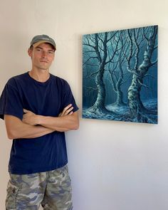 a man standing in front of a painting on the wall with his arms crossed next to him