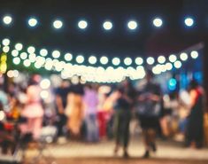 blurry image of people walking around at an outdoor event with lights in the background