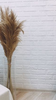 there is a vase with some dry grass in it next to a white brick wall