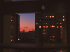 the view from an apartment window at night with buildings in the background and lights on